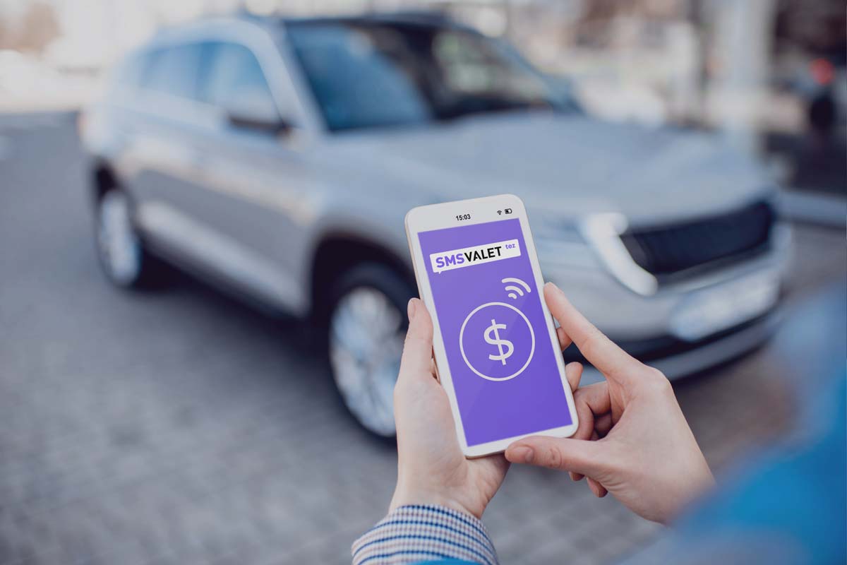 two hand holding mobile phone with car in background